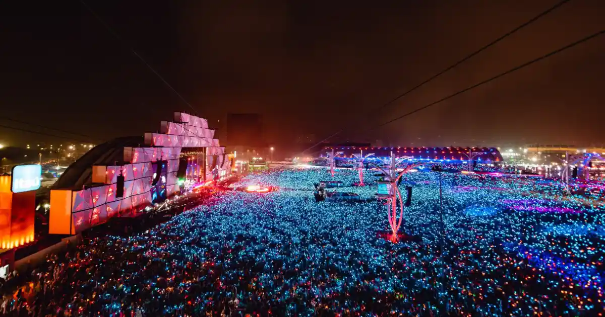 Foto da vista do Palco Mundo do Rock in Rio a partir da tirolesa do evento. Há diversas pessoas no festival e a foto está bem iluminada com bastante luz azul