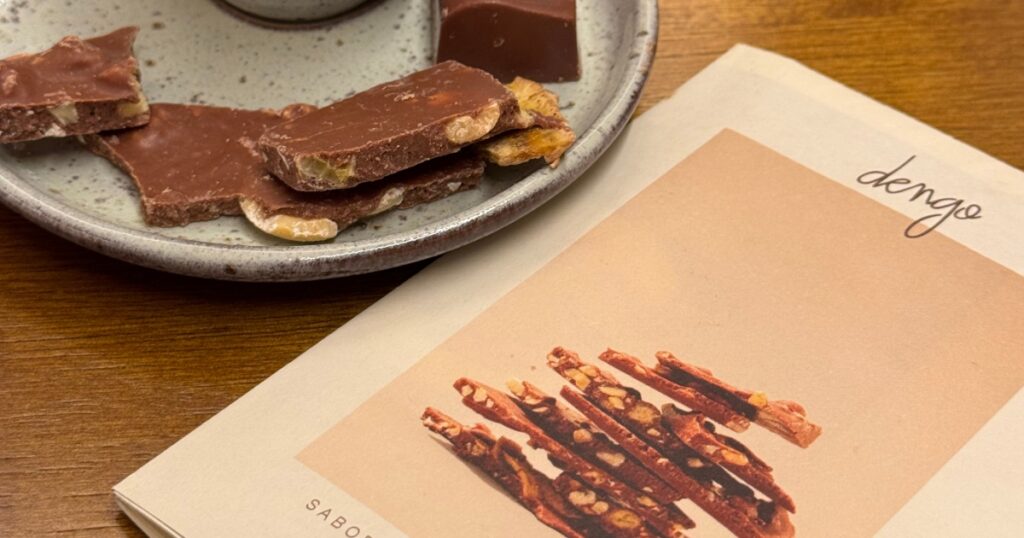 Foto de um panfleto da Dengo ao lado de um pequeno prato com alguns pedaços de chocolates